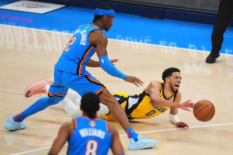 Tyrese Haliburton yells out and winces in pain as he lands horizontally on the court. Shai Gilgeous-Alexander leans over him