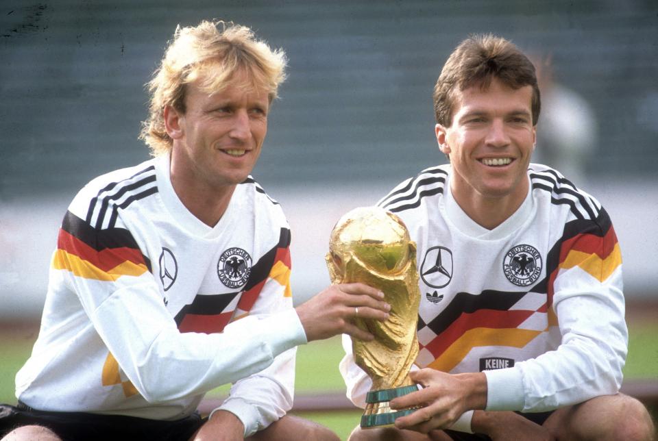 Andreas Brehme and Lothar Matthäus holding the World Cup trophy.