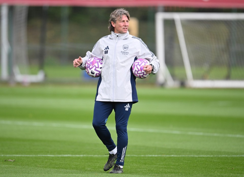 A man in an Arsenal tracksuit carrying two soccer balls.