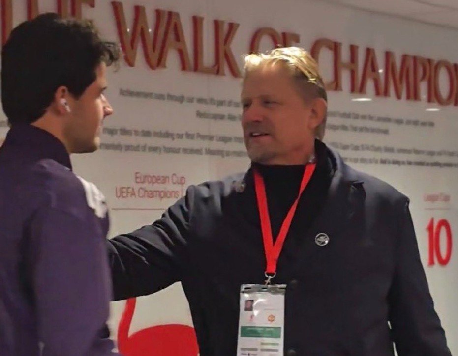 Peter Schmeichel and Senne Lammens in front of "The Walk of Champions" wall.