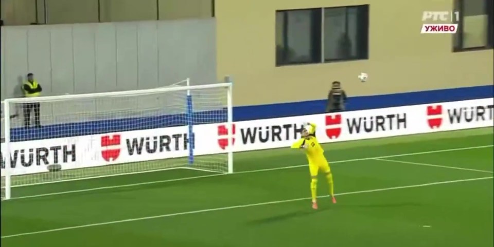 A football goalkeeper in a yellow uniform leaps for a high shot as the ball sails past him into the goal.