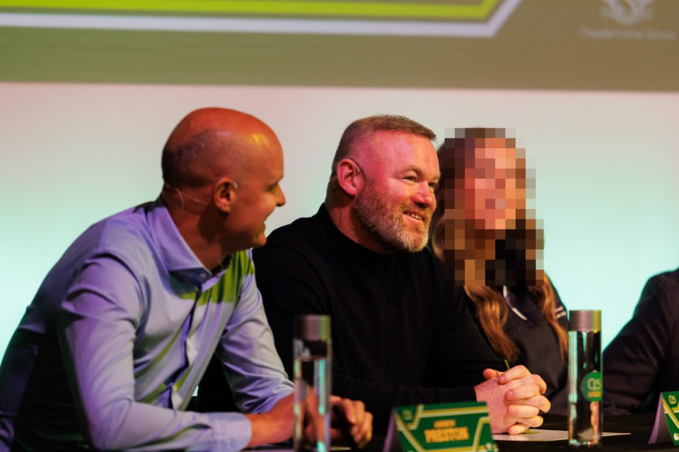 Wayne Rooney and another man smiling while sitting at a table with an obscured person.