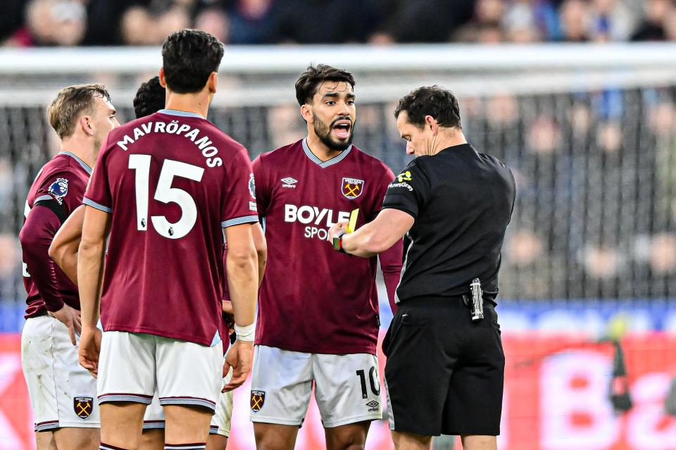 Lucas Paqueta argues with referee Darren England as the referee holds up a yellow card during a soccer match.