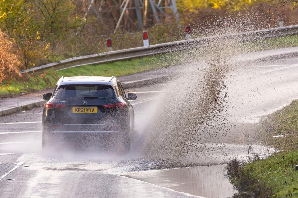 A car splashes through a puddle on a flooded road.