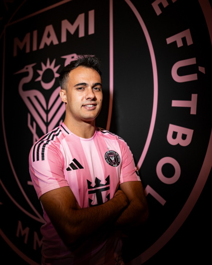 Man in a pink Inter Miami FC jersey, smiling with arms crossed.