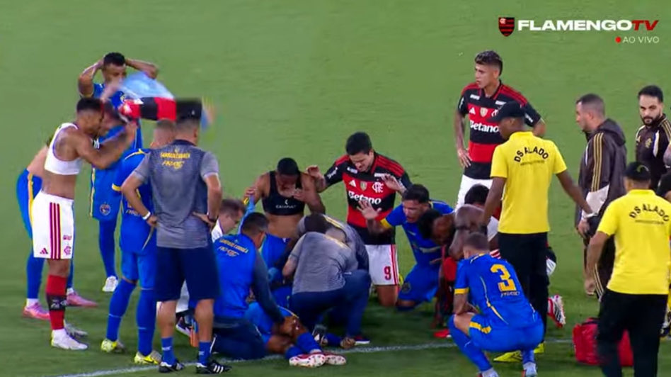 Football players and staff attending to a player who collapsed on the field after suffering a seizure.