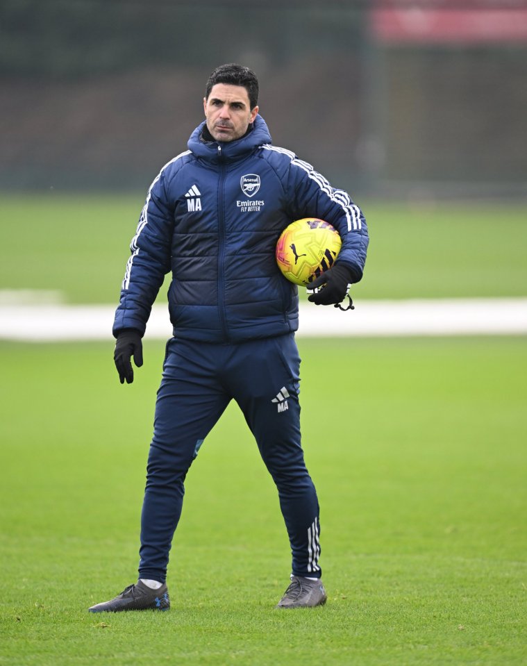 Mikel Arteta standing on a soccer field, holding a yellow soccer ball.
