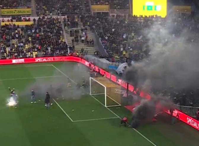 Soccer fans on the field among pyrotechnics and smoke.